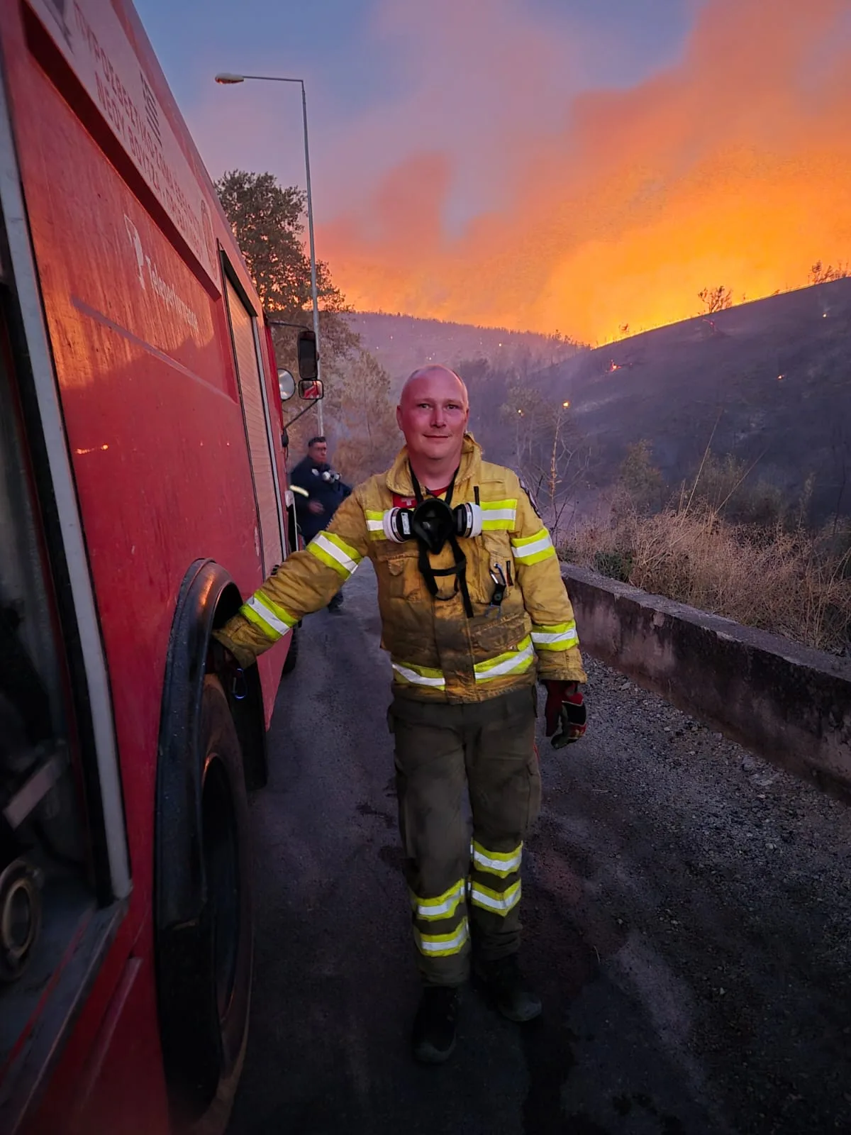 Ein Feuerwehrmann vor einem brennenden Hügel.